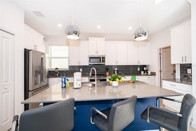 kitchen featuring appliances with stainless steel finishes, a kitchen island with sink, hanging light fixtures, and white cabinets