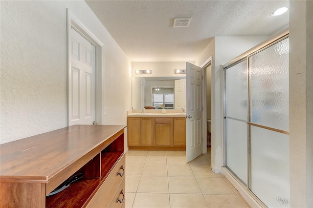 bathroom featuring tile patterned floors, a shower with door, vanity, and a textured ceiling