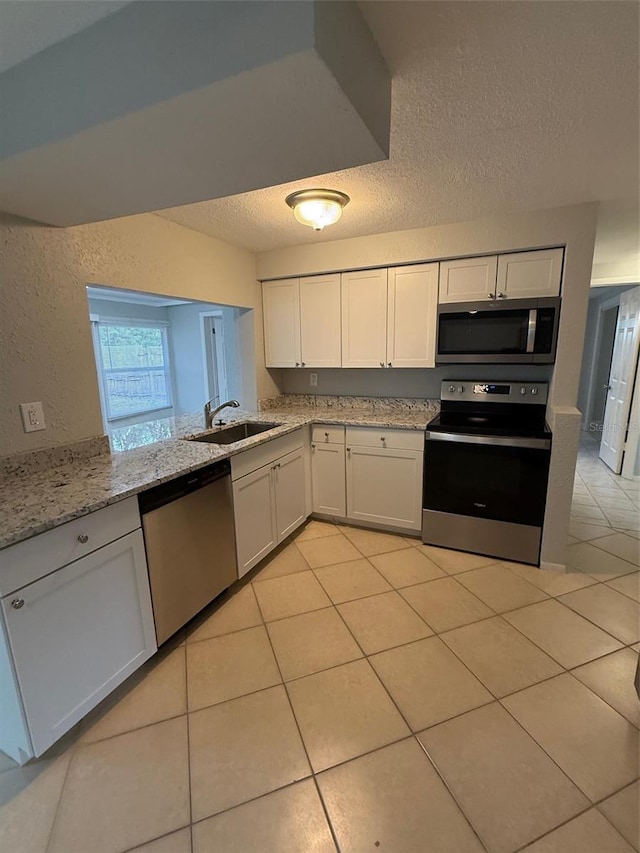 kitchen featuring sink, appliances with stainless steel finishes, light stone counters, a textured ceiling, and white cabinets