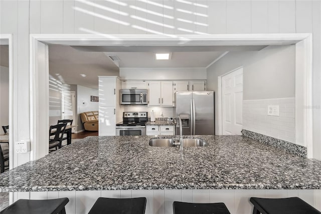 kitchen with sink, a breakfast bar area, appliances with stainless steel finishes, white cabinets, and dark stone counters