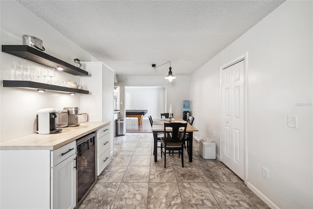 kitchen featuring pendant lighting, beverage cooler, a textured ceiling, and white cabinets