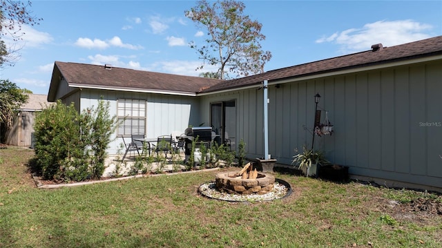 back of house with an outdoor fire pit and a lawn