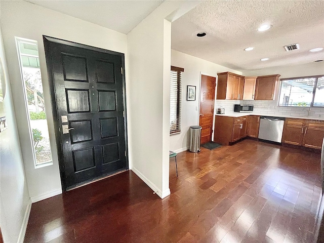 kitchen featuring dark wood-type flooring, visible vents, decorative backsplash, brown cabinets, and dishwasher