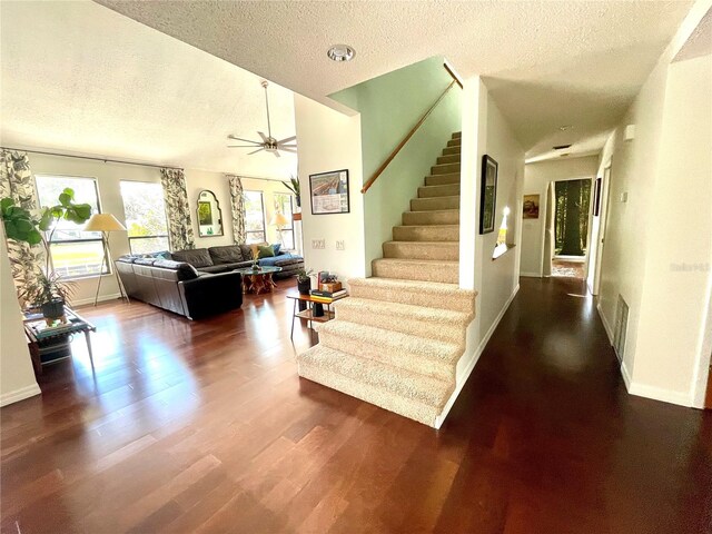 staircase featuring ceiling fan, a textured ceiling, baseboards, and wood finished floors