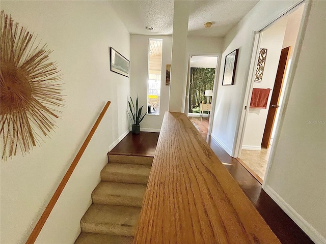 hall with a textured ceiling, baseboards, and wood finished floors