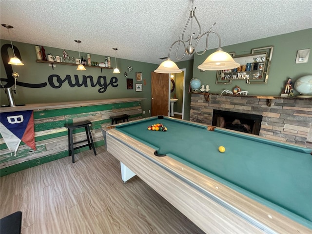 game room with a textured ceiling, a stone fireplace, wood finished floors, and billiards