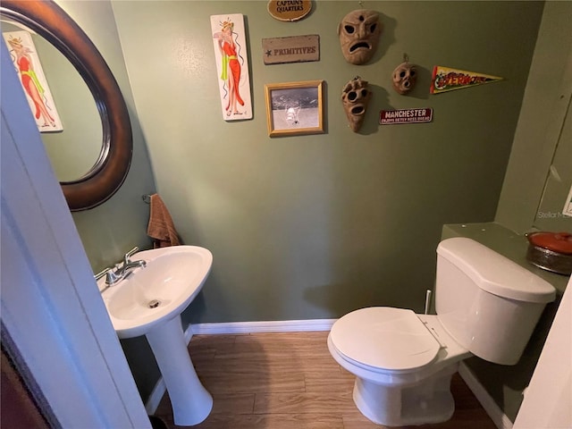 half bathroom with toilet, a sink, baseboards, and wood finished floors