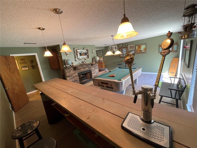 dining area with baseboards, a stone fireplace, a textured ceiling, and wood finished floors