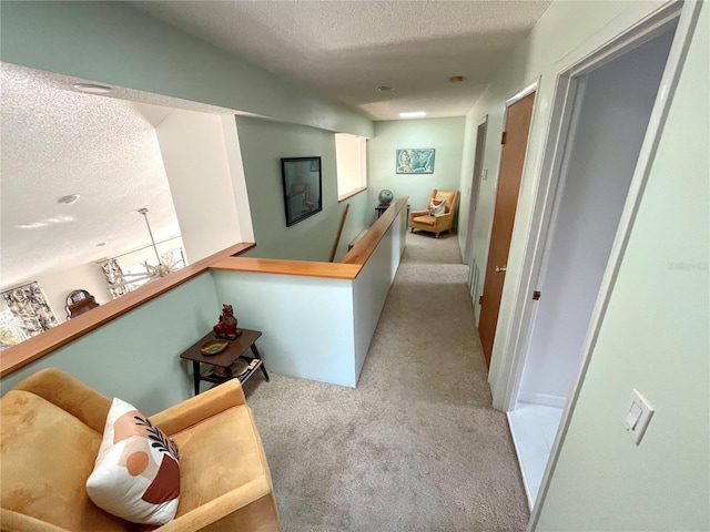 corridor featuring a textured ceiling, carpet flooring, and an upstairs landing