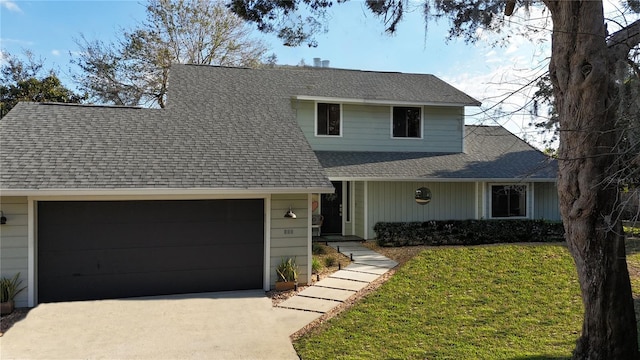 traditional-style house featuring a garage, driveway, a shingled roof, and a front yard