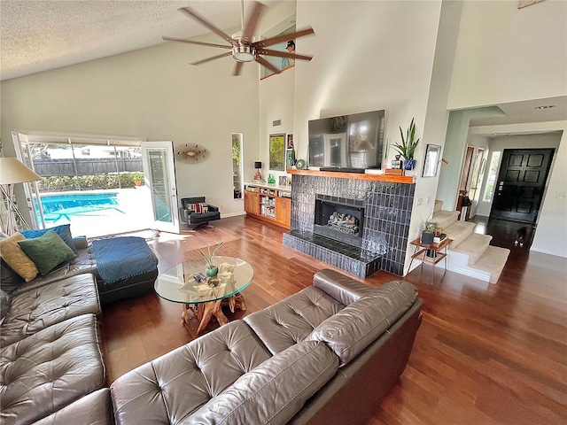 living area with a textured ceiling, lofted ceiling, wood finished floors, baseboards, and a tiled fireplace