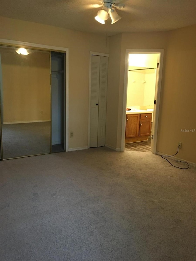 unfurnished bedroom featuring ceiling fan, two closets, light carpet, and ensuite bathroom