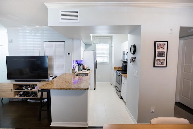 kitchen featuring sink, white cabinetry, stainless steel appliances, light stone counters, and a kitchen bar