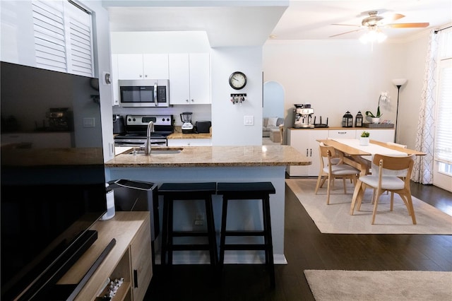 kitchen with dark hardwood / wood-style floors, sink, white cabinets, a kitchen bar, and stainless steel appliances