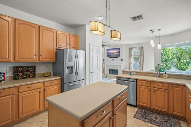 kitchen featuring a tile fireplace, a kitchen island, appliances with stainless steel finishes, decorative light fixtures, and sink