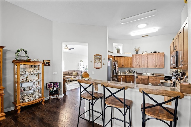 kitchen featuring kitchen peninsula, stainless steel appliances, a breakfast bar, ceiling fan, and dark wood-type flooring