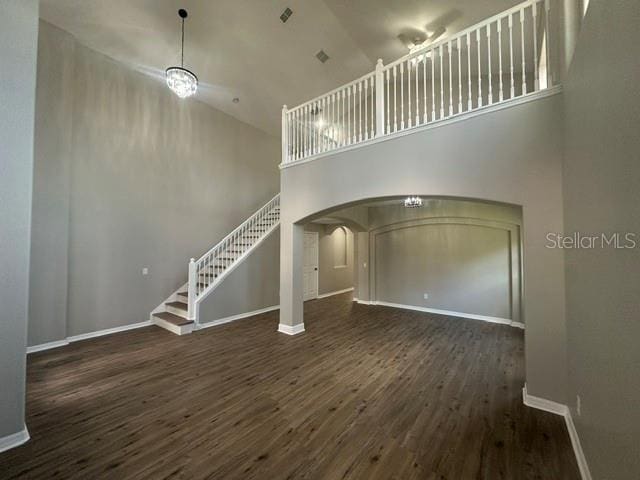 unfurnished living room featuring baseboards, arched walkways, a towering ceiling, dark wood-type flooring, and stairs