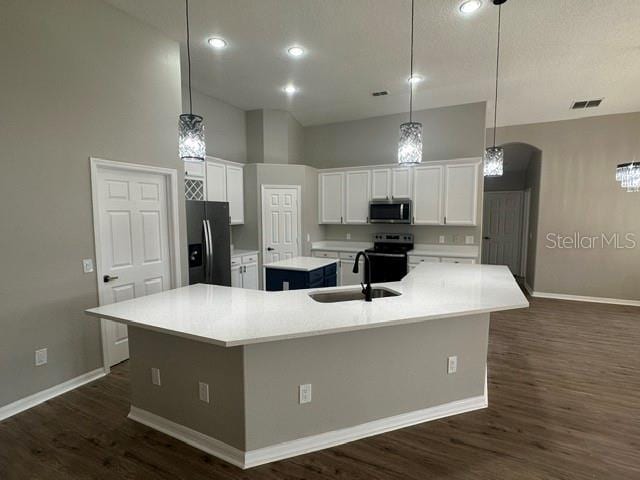 kitchen with light countertops, stainless steel microwave, white cabinetry, fridge with ice dispenser, and an island with sink