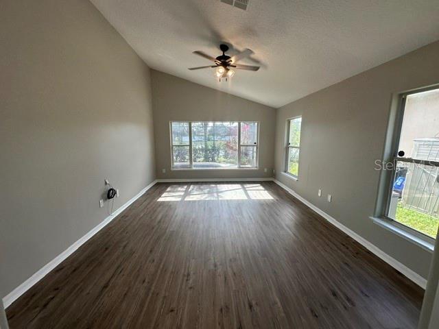 unfurnished room with a wealth of natural light, lofted ceiling, dark wood-style flooring, and baseboards