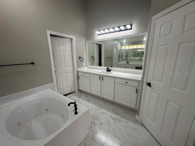 full bathroom featuring a whirlpool tub, marble finish floor, and vanity