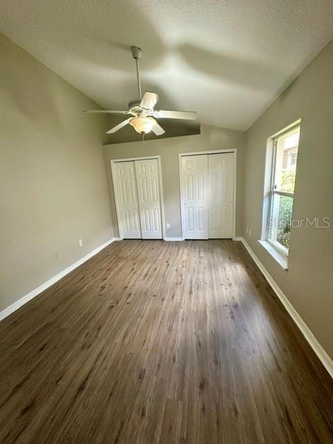 unfurnished bedroom featuring dark wood finished floors, vaulted ceiling, baseboards, and two closets