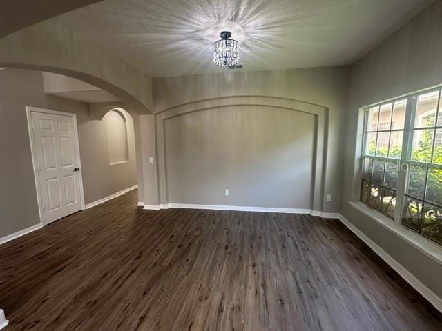 unfurnished room with arched walkways, dark wood-style flooring, and baseboards