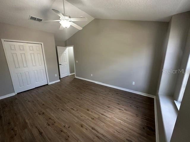 unfurnished bedroom with a closet, dark wood-type flooring, vaulted ceiling, a textured ceiling, and baseboards