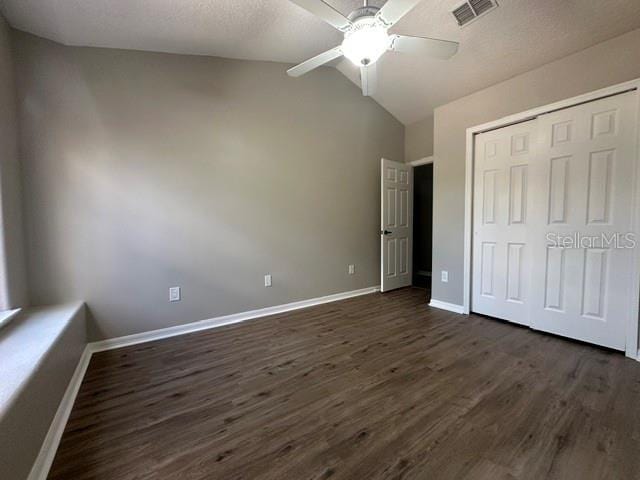 unfurnished bedroom featuring baseboards, visible vents, dark wood-style floors, vaulted ceiling, and a closet