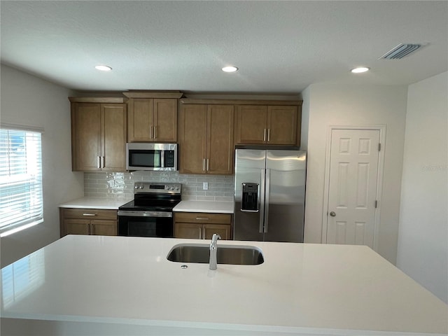 kitchen featuring tasteful backsplash, stainless steel appliances, a kitchen island with sink, and sink