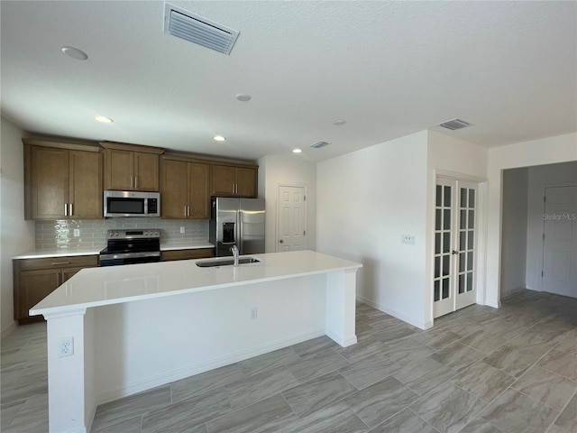 kitchen with french doors, sink, a center island with sink, appliances with stainless steel finishes, and decorative backsplash