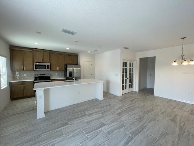 kitchen with appliances with stainless steel finishes, tasteful backsplash, sink, hanging light fixtures, and a kitchen island with sink