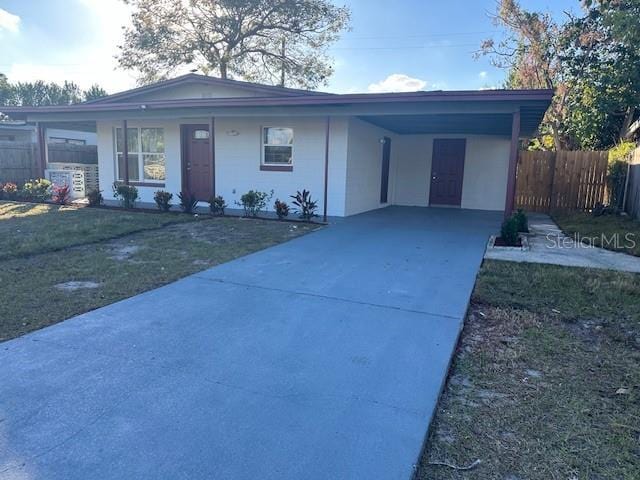 ranch-style home featuring concrete driveway, an attached carport, a front yard, and fence