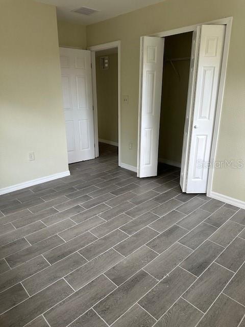 unfurnished bedroom with visible vents, baseboards, a closet, and wood finish floors