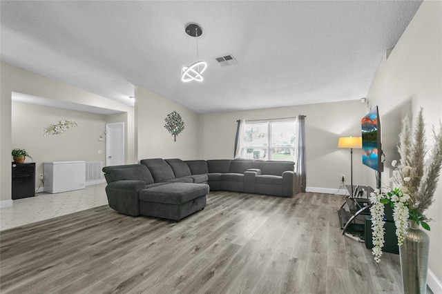 living room with baseboards, a textured ceiling, visible vents, and wood finished floors