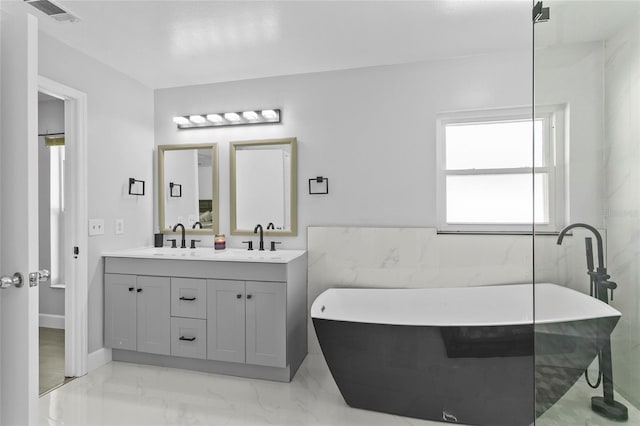 full bath featuring double vanity, a freestanding bath, visible vents, and a sink