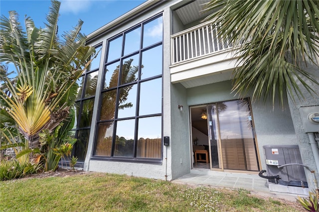 property entrance with central AC unit, a balcony, and a lawn