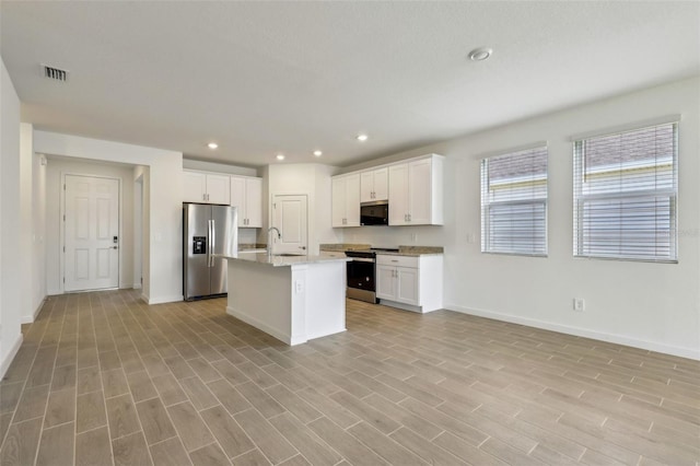 kitchen with stainless steel appliances, a sink, open floor plan, baseboards, and white cabinetry
