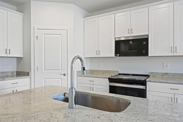 kitchen with light stone counters, a sink, black microwave, stainless steel electric range, and white cabinetry