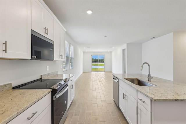 kitchen featuring a sink, light wood-style floors, light stone countertops, appliances with stainless steel finishes, and white cabinetry