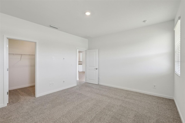unfurnished bedroom featuring a spacious closet, carpet, visible vents, and baseboards