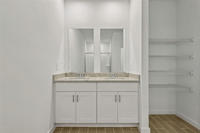 bathroom with wood finish floors, a sink, double vanity, and baseboards
