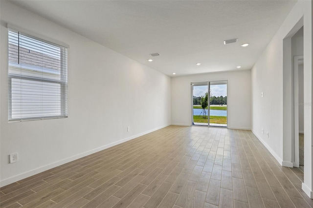 empty room with wood finished floors, visible vents, and baseboards