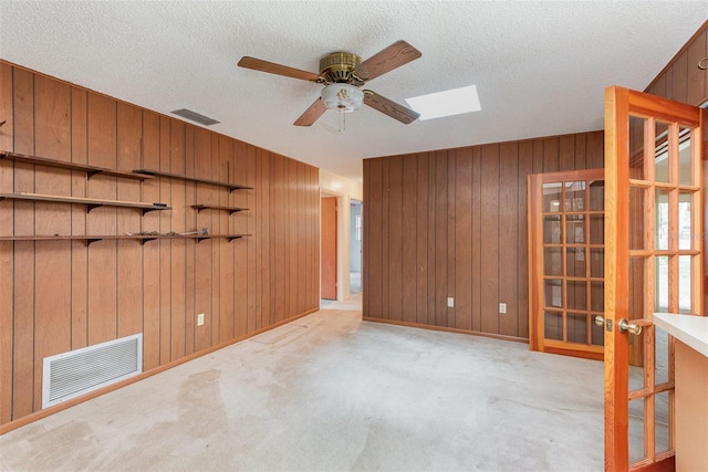 empty room with ceiling fan, a textured ceiling, light colored carpet, french doors, and wood walls