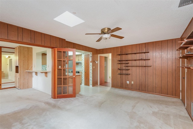 carpeted empty room with a skylight, a textured ceiling, wooden walls, and ceiling fan