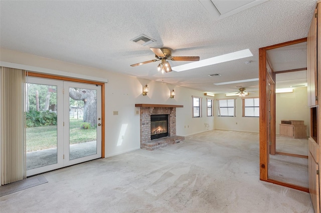 unfurnished living room featuring a brick fireplace, light colored carpet, a textured ceiling, and ceiling fan