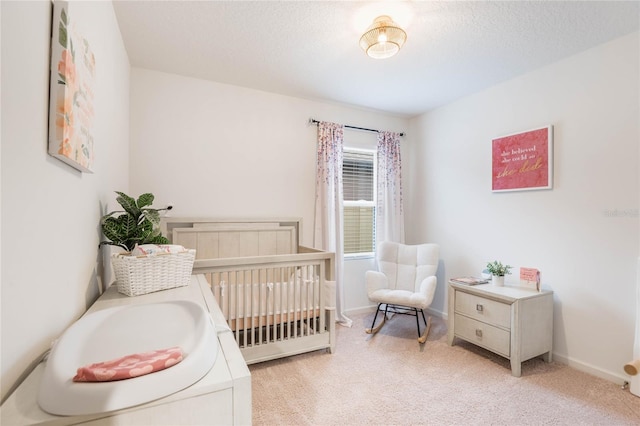 bedroom with a nursery area, light colored carpet, a textured ceiling, and baseboards