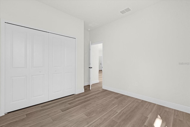 unfurnished bedroom with light wood-style flooring, a closet, visible vents, and baseboards