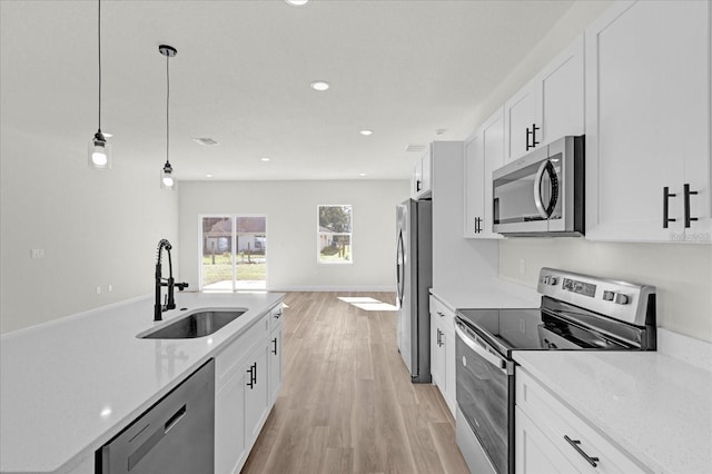 kitchen with hanging light fixtures, stainless steel appliances, light wood-style floors, white cabinetry, and a sink