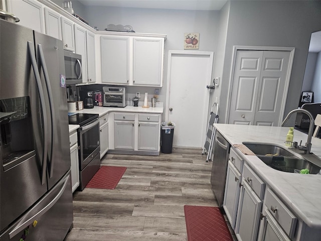 kitchen with sink, white cabinetry, stainless steel appliances, light stone counters, and light hardwood / wood-style floors