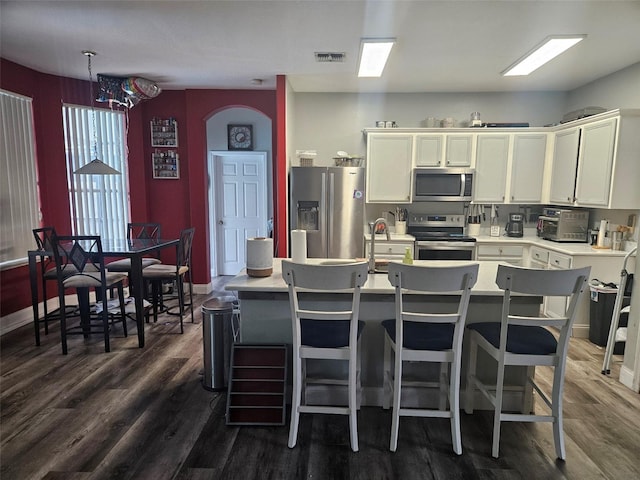 kitchen featuring appliances with stainless steel finishes, dark hardwood / wood-style flooring, and an island with sink